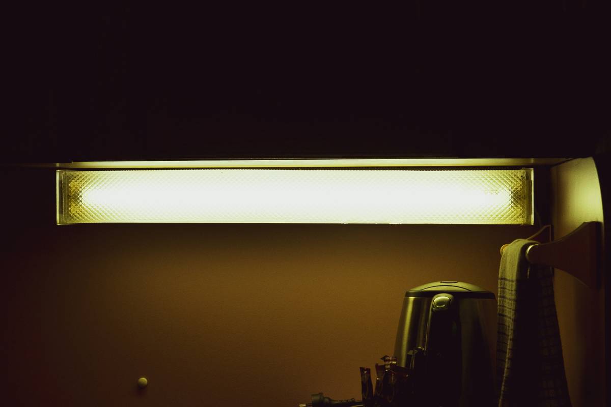 Side-by-side comparison: left shows harsh overhead lighting casting unflattering shadows; right shows warm sconces creating even, inviting glow around mirror