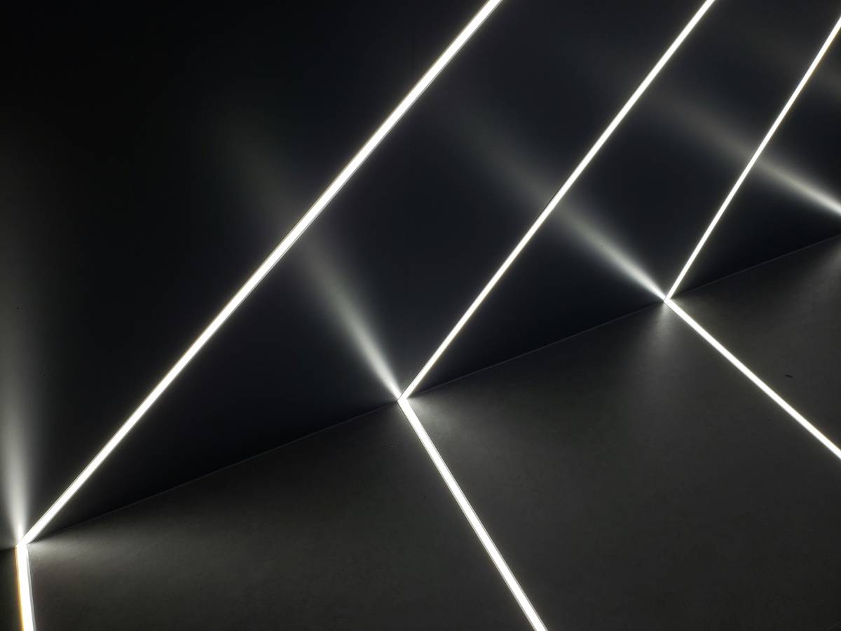 Side-by-side comparison: left shows uneven puck lighting with hotspots, right shows smooth, diffused glow from a linear LED light bar behind glass shelves